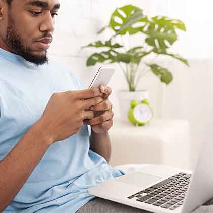 Man sitting at a laptop looking at a cell phone