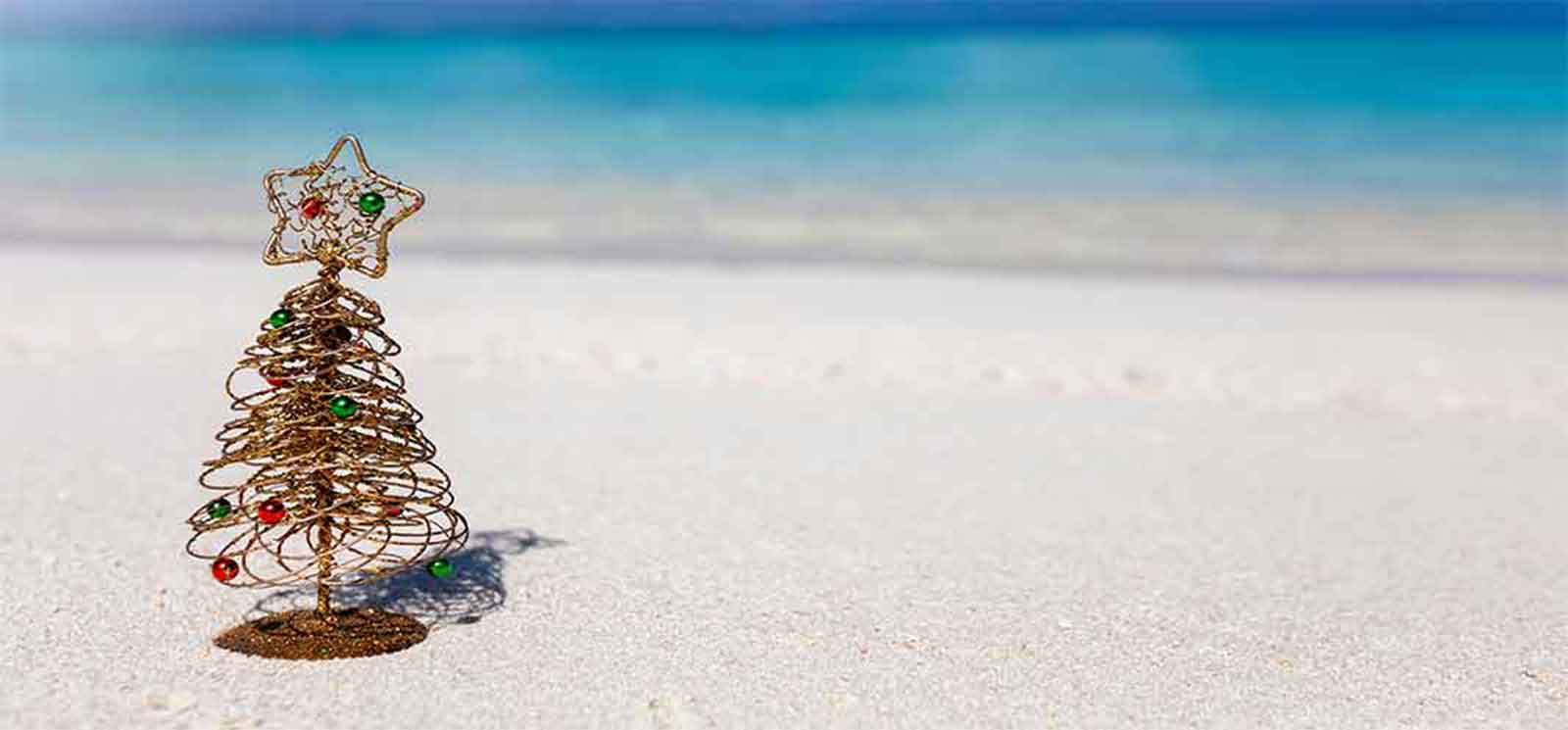 Copper wire Christmas tree on a white beach and blue ocean